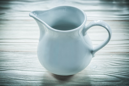 White ceramic milk jug on wooden board.