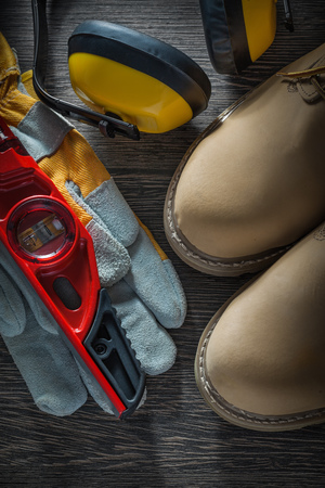 Earmuffs protective gloves boots construction level on wooden board.の写真素材