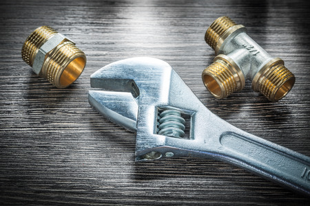 Adjustable wrench threaded pipe fittings on wooden board.