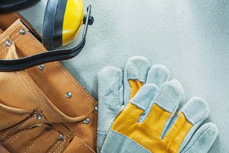 Leather construction belt protective gloves earmuffs on concrete background.
