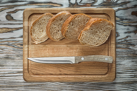 Chopping board knife sliced bread on wooden surface.