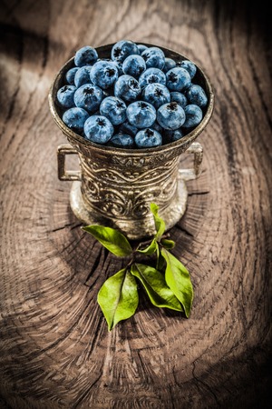 Ripe bilberries in vintage metal bowl on grunge board.の写真素材