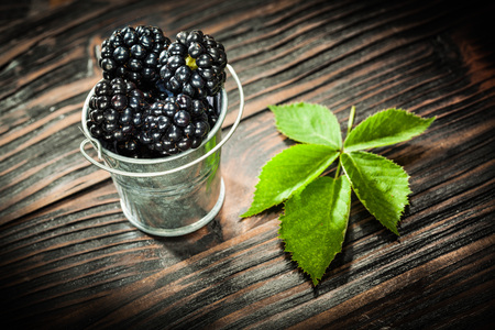 Dewberries in bucket on vintage wooden board.