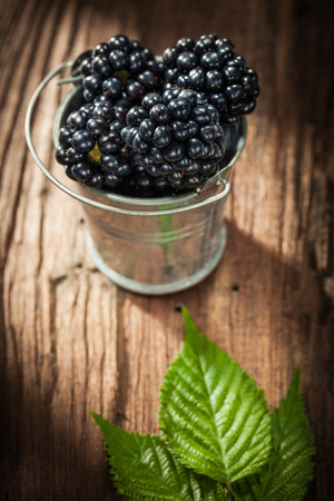 Juicy blackberries in bucket on vintage wooden board.の写真素材
