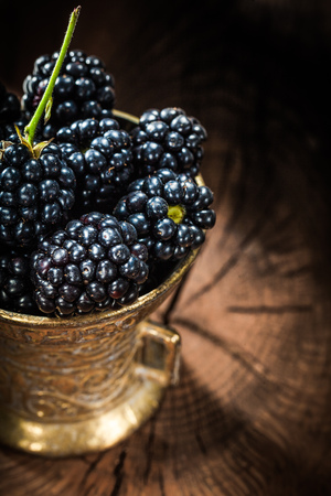 Sweet blackberries in metal bowl on vintage wooden board.の写真素材