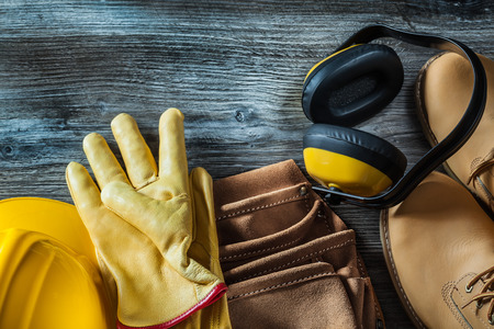 Leather protective gloves boots tool belt hard hat earmuffs on wooden board.の写真素材