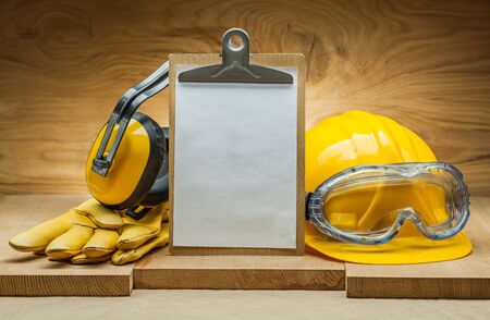 safety concept. blank sheet of paper for copyspace in clipboard. construction helmet and goggles yellow leather gloves earphonesの写真素材