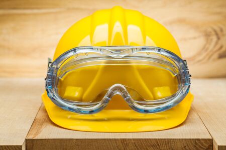 safety tools. yellow construction helmet with blue goggles on wooden boardの写真素材
