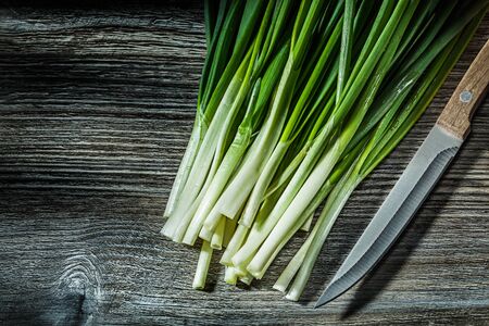 bunch of green scallions and kitchen knife on vintage woodの写真素材