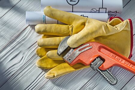 big monkey wrench in yellow leather glove and rolled blueprints on vintage white wood