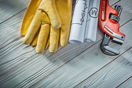 plumbing engineering rolled piping blueprints pipe wrench yellow leather work gloves on vintage white wood backgroundの写真素材
