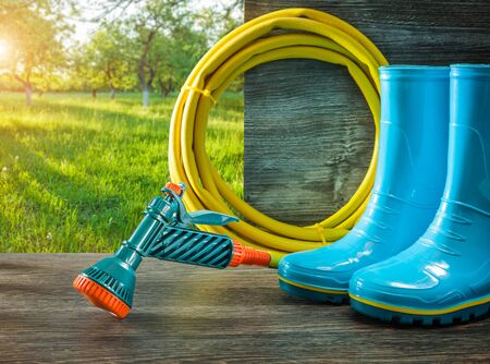 gardening tools watering hose with spray gan rain rubber boots on terrace in spring sunny gardenの写真素材
