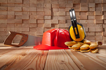 Red Construction Helmet Yellow Protective Earphones Leater Working Gloves Classic Handsaw With Wooden Handle. On Background Of Wooden Beams Stackの写真素材