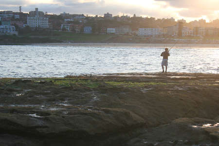 Fisherman fishing on Bondi Beach during winter. Beautiful sunlight.の写真素材