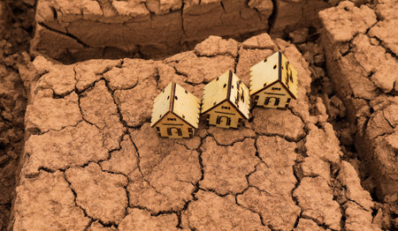 Wooden toy house on cracked earth background. The concept of climate changeの写真素材