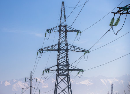 High-voltage tower against the blue sky and snow-capped mountainsの写真素材