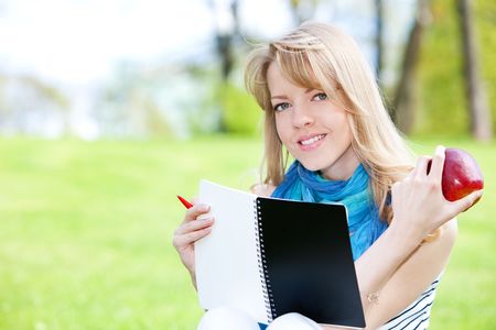 Pretty girl studying on a green meadow with notebookの写真素材