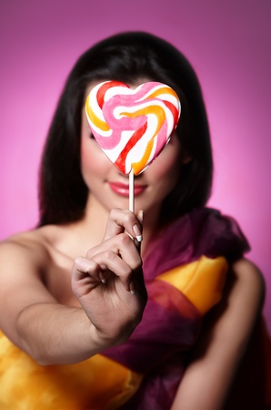 Portrait of a girl holding lollypop in front of her. Focus is on the lollypop.の写真素材