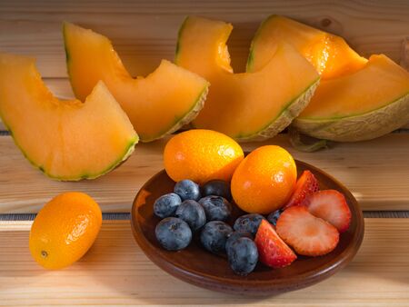 Close up view of blueberries and strawberries and melon and kumquat on a wooden background illuminated by sunlight.の写真素材