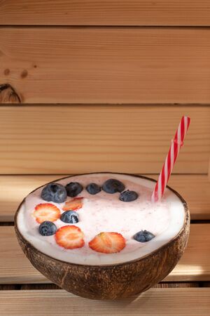 View of strawberry smoothie in a coconut bowl with blueberries on a wooden background. Soft focus. Vertical orientation. With copy space.の写真素材