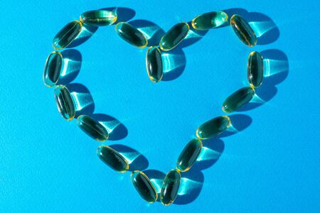 Top view of the figure of heart from Omega 3 capsules with a reflection on blue backgroundの写真素材