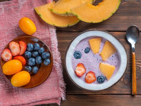 Top view of blueberry smoothie in a coconut bowl with strawberries and melon and kumquat on a red towel with a teaspoonの写真素材