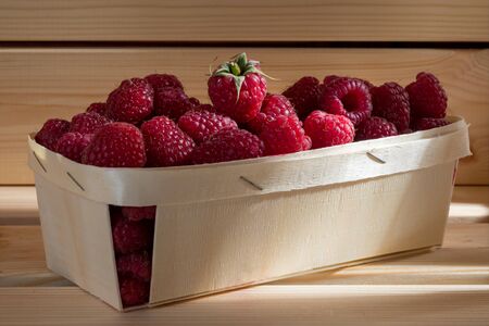 Wooden box of fresh raspberries on white wooden background. Selective focus