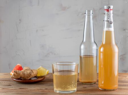 Two bottles and glass of kombucha drink on a wooden table with a ginger and a slice of grapefruit on the plate.の写真素材