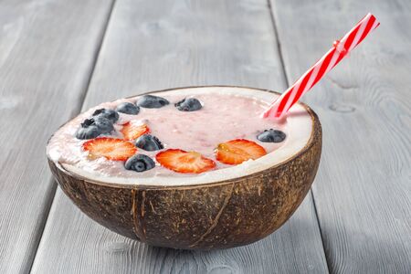 View of strawberry smoothie in a coconut bowl with blueberries on a white wooden background.の写真素材