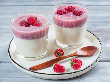 Top view of two cups of panna cotta with a teaspoon of the white rustic plate. White wooden background.の写真素材