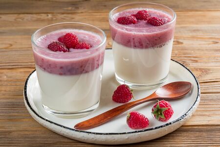 Two cups of panna cotta with a teaspoon of the white rustic plate. Wooden background.の写真素材