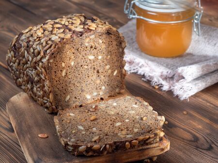 Close up View of Brown Homemade Bread with a glass jar of honey on wooden background illuminated by sunlight. Selective focus.の写真素材