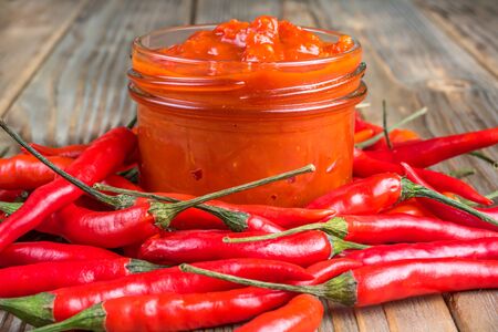 Glass jar of harissa surrounded by hot chili pepper on wooden backgroundの写真素材