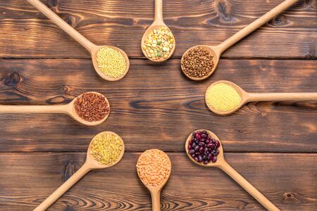 View of different types of grains and cereals in wooden spoons on wooden backgroundの写真素材