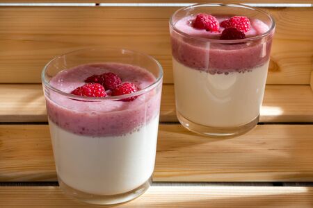 Two cups of panna cotta with a raspberry on wooden background Illuminated by sunlight.の写真素材