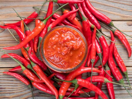 Top Close up view of a glass jar of harissa surrounded by hot chili pepper on wooden backgroundの写真素材