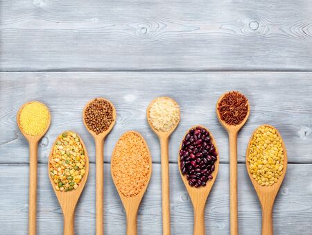 Top view of different types of grains and cereals in wooden spoons on a white wooden background. With copy space.の写真素材