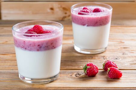 Two cups of panna cotta with a raspberry on wooden background.の写真素材