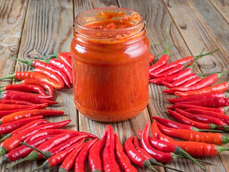 hot chili pepper lay around of glass jar of harissa on wooden backgroundの写真素材