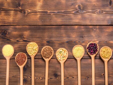 Top view of different types of grains and cereals in wooden spoons on wooden background.の写真素材