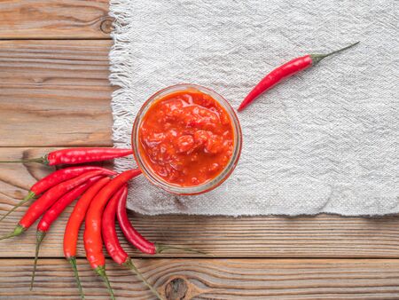 Glass jar of harissa surrounded by hot chili pepper on a white linen towelの写真素材