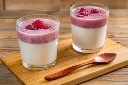 Two cups of panna cotta with a teaspoon on wooden background Illuminated by sunlight.の写真素材