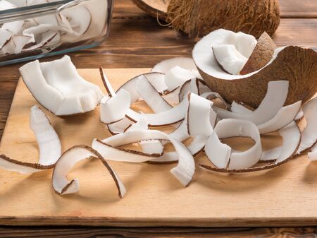 Close up view of dried coconut chips in on baking paper in a glass pan and on cutting board with coconut shellsの写真素材