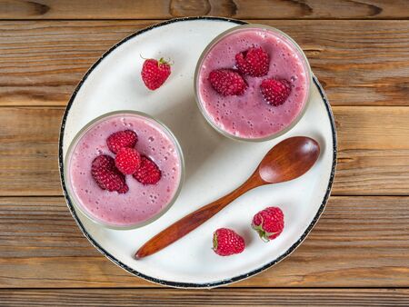 Top view of two cups of panna cotta with a teaspoon of the white rustic plate. Wooden background.の写真素材