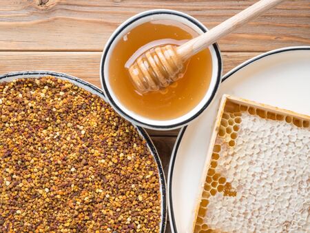 The dish with bee pollen on and honeycombs and cup of honey wooden backgroundの写真素材
