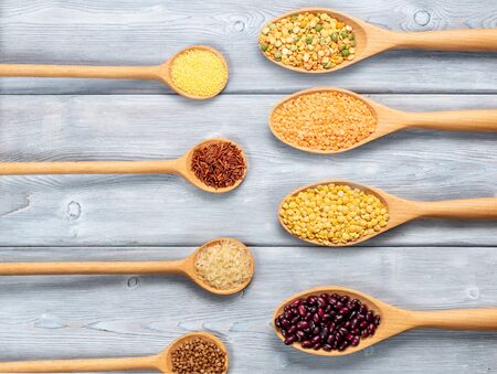 Top view of different types of grains and cereals in wooden spoons on a white wooden backgroundの写真素材
