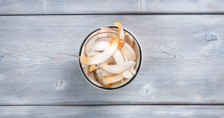 Top view of dried coconut chips in white bowl on white wooden backgroundの写真素材