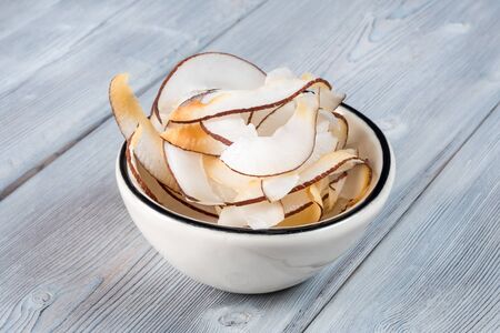 View of Dried coconut chips in white bowl on white wooden backgroundの写真素材