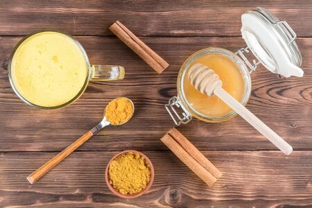 Top view of a cup of golden milk with turmeric and cinnamon and wooden spoon and honey on a wooden backgroundの写真素材