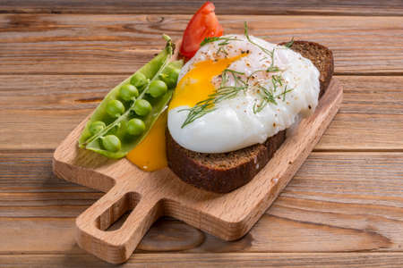 Close up view of poached egg on the sandwich with onion and peas and tomato on wooden background. soft focusの写真素材